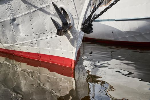 Nasal part of a sailing frigate of white color with an anchor on a nose, bright reflection in water. High quality photo