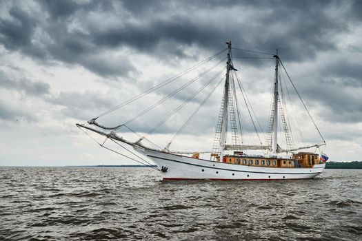 Antique sailing frigate of white color to the sea, the lowering storm sky, sails are lowered, masts and ropes. High quality photo