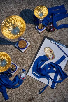 Russia.Petersburg, 05 September 2020: Gold cups and medals of winners expect the delivery, blue ribbons, results of race of sailboats, the top view. High quality photo