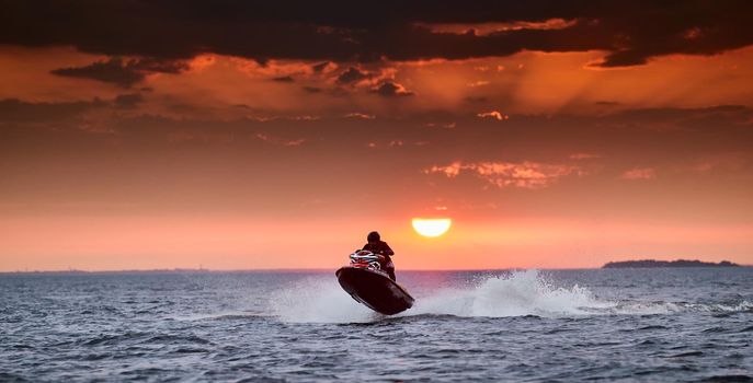 Russia, St.Petersburg, 06 September 2020:The person on a hydrocycle in flight over water on a sunset, splashes from under a hydrocycle, the sun on the horizon. High quality photo