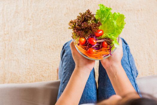 Young woman eating fresh salad meal vegetarian spinach in a bowl, top view of female hands holding bowl with green lettuce salad on legs, Clean detox healthy food concept