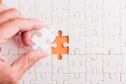 Top view flat lay of hand-holding last piece white paper jigsaw puzzle game last pieces put to place for solve problem complete mission, studio shot on an orange background, quiz calculation concept