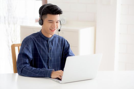 Young asian businessman working on laptop computer wearing headphone at home, business man wearing headset for video conference, communication and education, male study and learning for e-learning.