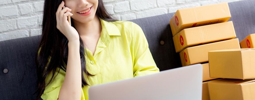 Young asian woman is entrepreneur talking with customer and using laptop computer while order purchase online at home, logistic and delivery, online shopping, female is seller of business SME.