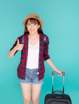 Beautiful young asian woman pulling suitcase isolated on blue background, asia girl cheerful holding luggage walking and gesture thumbs up in vacation with excited, journey and travel concept.