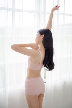 Beautiful young asian woman waking up in the morning stand stretching arms in the bedroom, sexy girl in underwear relax cozy and wake with fresh happy at home, lifestyle concept, back view.