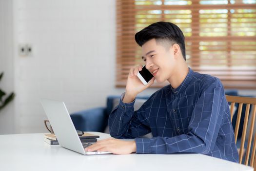 Young asian man talking phone and work from home with laptop computer, freelance using notebook to internet online and speak on smartphone, domestic life, business and communication concept.