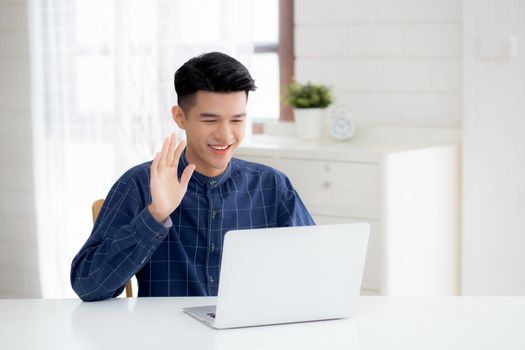 Young asian business man using laptop computer for video call online hello and communicate work from home, male conference with notebook and say hi, social distancing, communication concept.