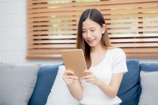 Young attractive asian woman resting using browsing tablet computer on sofa at home, happy girl sitting on couch relax reading digital gadget at house, communication and lifestyle concept.