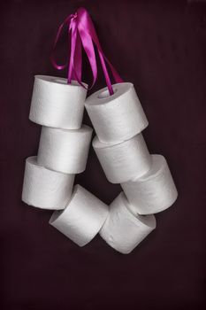 On a dark background, a roll of white toilet paper is connected by a ribbon in a bundle. Front view, vertical orientation