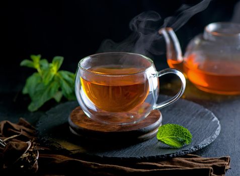 Teapot with tea surrounded with green leaves, tea ceremony, green tea in a transparent cup