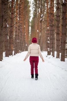 Winter walk in a snow-covered forest, A girl with a red jumpsuit and jacket walks among tall trees in nature. Solitude and relaxation from the hustle and bustle of the city.