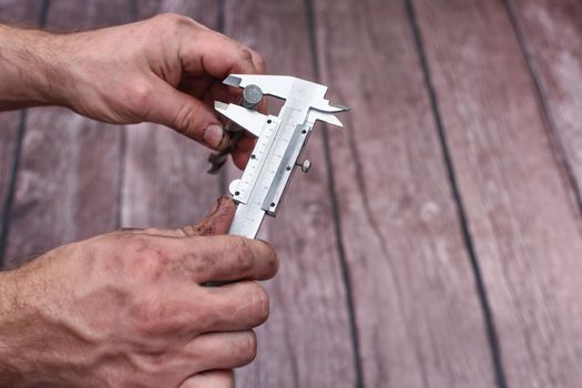 Measuring the drill diameter with a caliper. Hands are dirty while working. Close-up. on a wooden background.