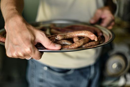 The guy carries raw sausages for the grill in a deep plate, close up shot