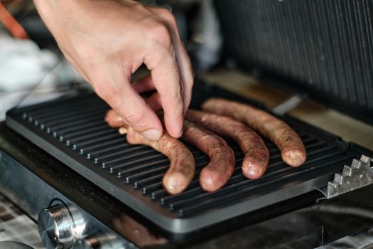 Man's hand lays out raw sausages on the grill, close up shot