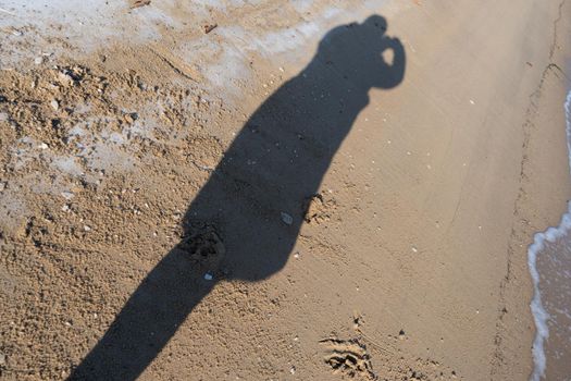 Background with the shadow of a man on the sand. Silhouette of a woman photographer.