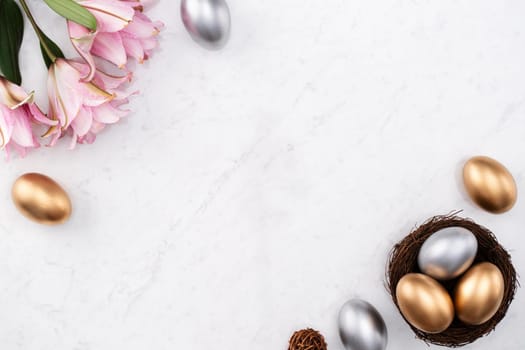 Design concept of Golden and silver Easter eggs in the nest with pink lily flower on bright marble white table background.
