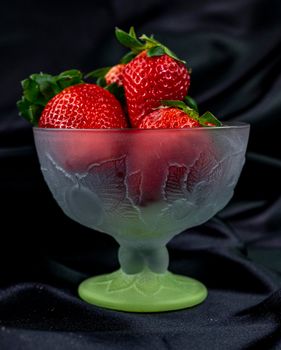 cup of ripe strawberries on black satin fabric background