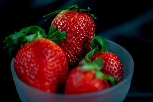 cup of ripe strawberries on black satin fabric background