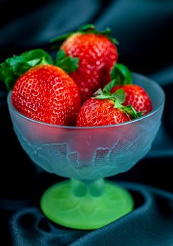 cup of ripe strawberries on black satin fabric background