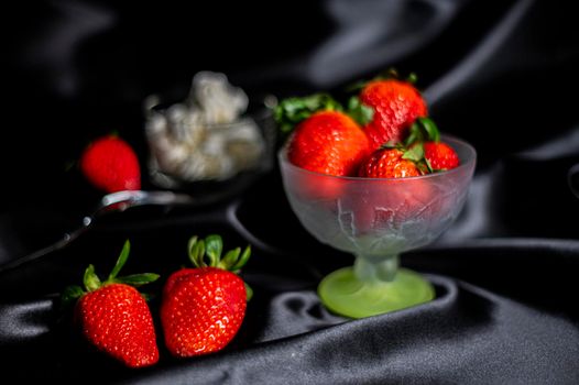 cup of ripe strawberries on black background with fork and cream