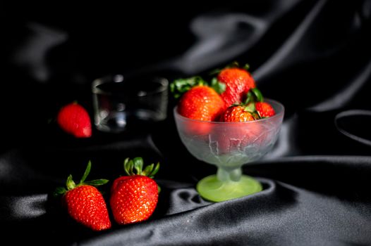 cup of ripe strawberries on black satin fabric background