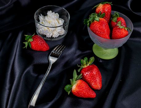 cup of ripe strawberries on black background with fork and cream