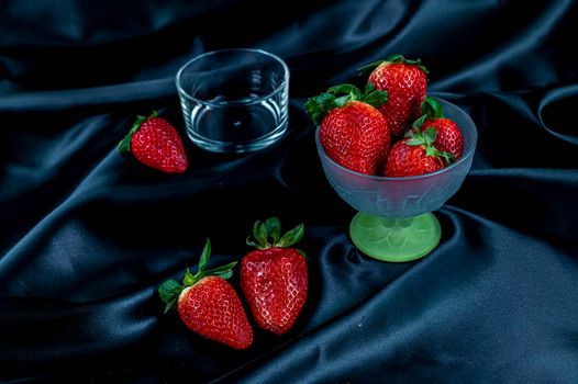 cup of ripe strawberries on black satin fabric background