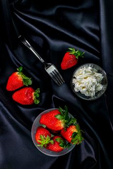 cup of ripe strawberries on black background with fork and cream