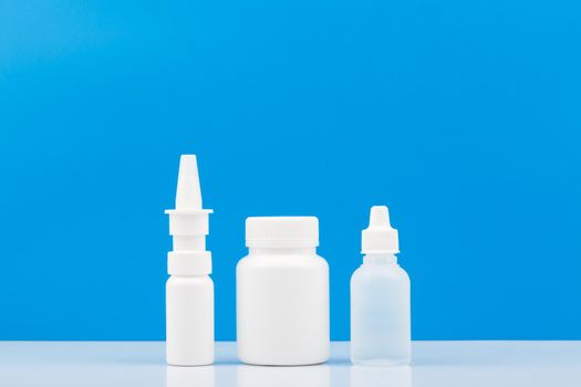 Nose spray, medication bottle and eye drops on white table against blue background with copy space. Concept of medical treatment of flue and virus disease