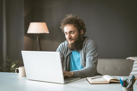 The copywriter works from home to write the article. A young man with curly hair is typing on a laptop. Work at home is a concept. High quality photo