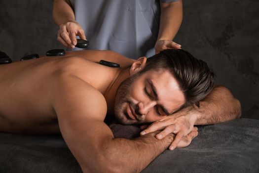 A good-looking man getting hot stone massage lying down at spa