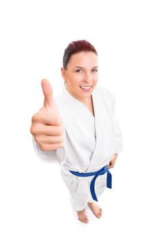Top-down full body portrait of a beautiful smiling young female fighter in white kimono and blue belt showing thumb up gesture, isolated on white background. Martial arts concept.