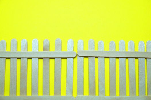 wooden ice cream sticks imitating a fence on a yellow background blank, copy space