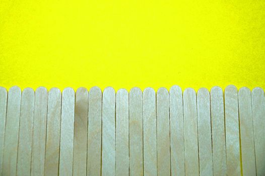 wooden ice cream sticks imitating a fence on a yellow background blank, copy space