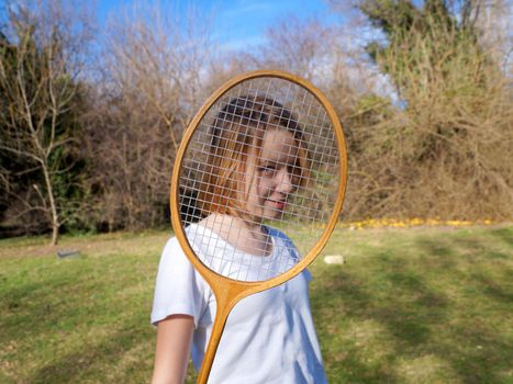 teenage girl looking through badminton racket and smiling.