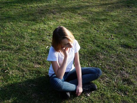 sad pensive teenage girl sitting on the grass in the park.