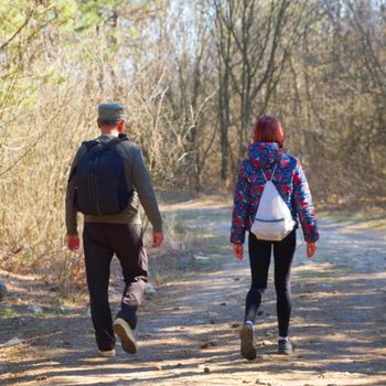 a man and a teenage girl are walking with backpacks along a forest road on a sunny day, back view