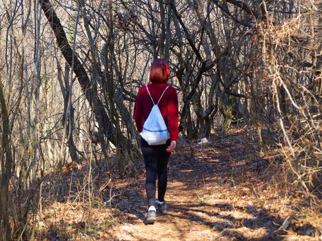 teenage girl in headphones goes along a forest trail with a backpack, back view