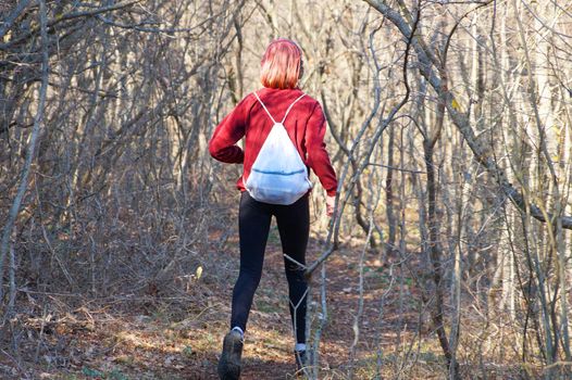 teenage girl in headphones goes along a forest trail with a backpack, back view
