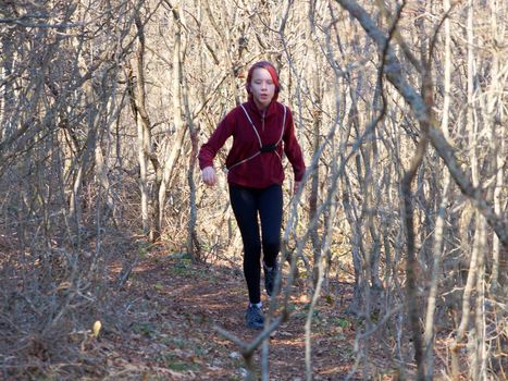 teenage girl in headphones runs along a forest trail with a backpack.