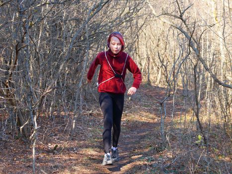 teenage girl in headphones runs along a forest trail with a backpack.