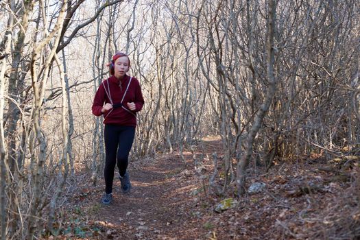 teenage girl in headphones runs along a forest trail with a backpack.