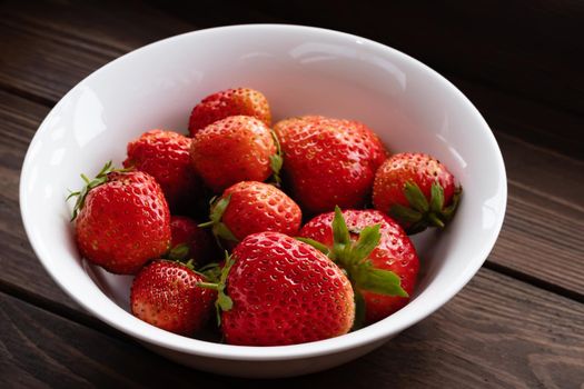 Natural ripe strawberries in a plain white bowl on a dark wooden table.