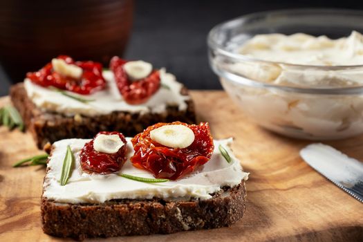 Homemade multigrain bread sandwiches with cream cheese and sun-dried tomatoes on a wooden platter, close-up. Healthy eating concept.