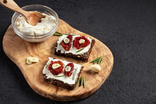 Homemade multigrain bread sandwiches with cream cheese and sun-dried tomatoes on a wooden platter. Healthy eating concept, copy space.