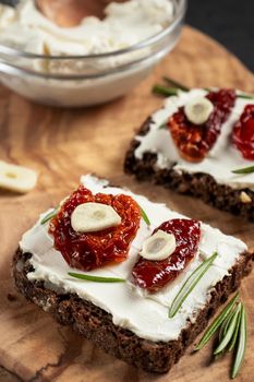 Homemade multigrain bread sandwiches with cream cheese and sun-dried tomatoes on a wooden platter. Healthy eating concept. Vertical image.