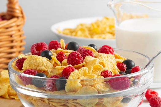 Glass bowl with cereal flakes and berries and milk on the table, close-up. Healthy summer breakfast.