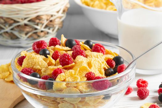 Glass bowl with cereal flakes and berries and milk on the table, close-up. Healthy summer breakfast.