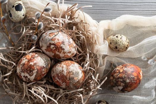 Easter composition - several marble eggs painted with natural dyes in a paper nest on the table, top view.